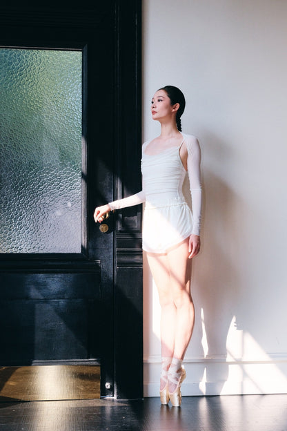Side view of Bloom Overlap Dance Shorts in dawn white, showing the curved overlap panel crossing at the hip