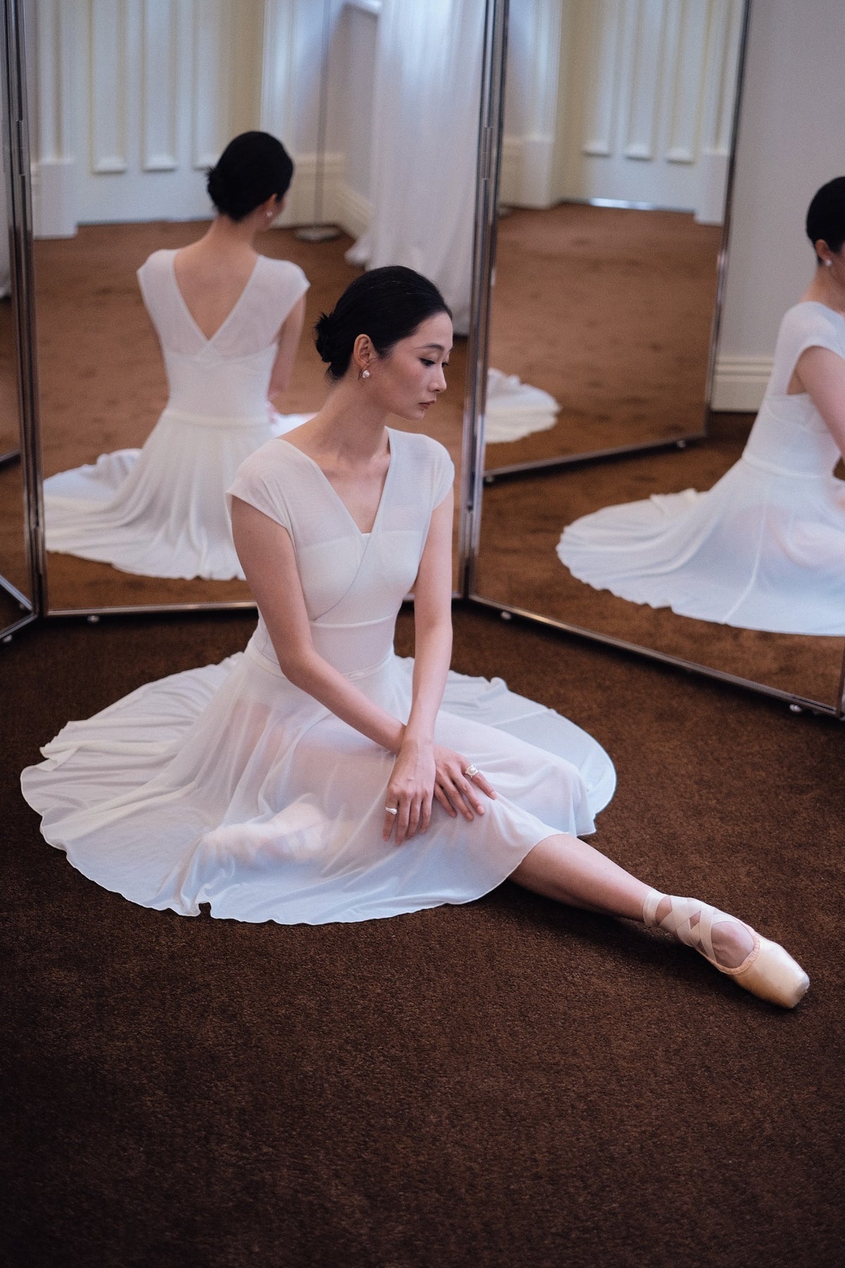 Dancer seated on the studio floor in a Dawn White Pull-On Full-Circle Ballet Rehearsal Skirt, the full-circle mesh spread out around her