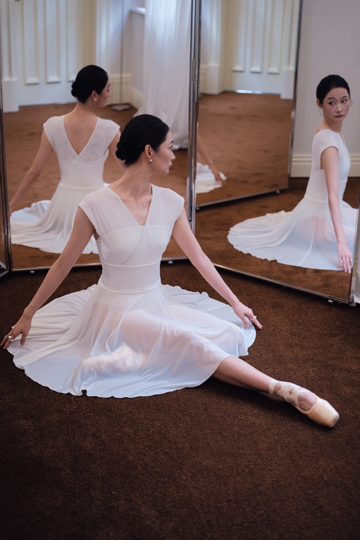 Dancer seated in a Dawn White Pull-On Full-Circle Ballet Rehearsal Skirt, the full-circle mesh sweeping across the studio floor